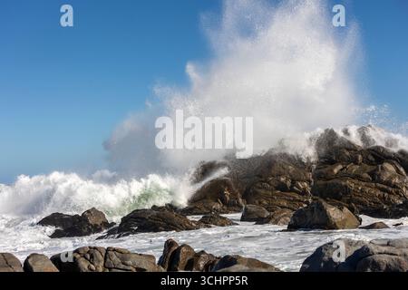 Big Ocean Wave s'écrase contre Rock avec éclaboussure spectaculaire montrant la puissance de la mer sous ciel bleu clair et littoral rocheux - paysage Banque D'Images