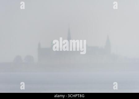 Château de Kronborg à travers la brume Helsingør Danemark / Helsingør, Danemark — le château de Kronborg est partiellement obscurci par une brume dense, créant une vue d'ambiance sur le site du patrimoine mondial de l'UNESCO. Situé à la pointe nord-est de l'île de Zélande, le château surplombe le détroit de Øresund. Réputé pour son association avec le hameau de William Shakespeare, le château a été construit par le roi Frédéric II entre 1574 et 1585 sur le site de la forteresse médiévale antérieure de Krogen. Kronborg est un exemple significatif de l'architecture militaire de la Renaissance et un point de repère important au Danemark. Banque D'Images