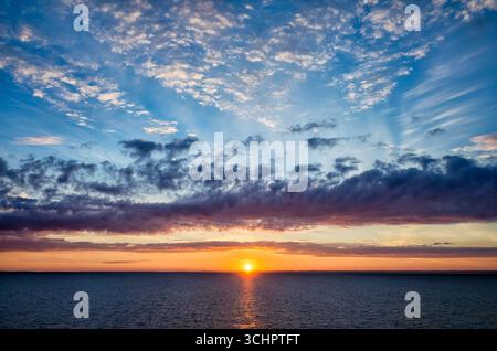 Lever de soleil sur la côte suédoise de Copenhague à Oslo Ferry Strömstad Suède // Strömstad, Suède — Un lever de soleil vibrant illumine le ciel sur les eaux au large de la côte suédoise près de Strömstad. La scène capture la transition de la nuit au jour, avec le soleil qui monte juste à l'horizon, projetant une lueur chaude à travers la mer. Des nuages tordus sont dispersés à travers l'étendue bleue, certains teintés de teintes orange et violettes du soleil levant. Cette vue est caractéristique du paysage côtier de la région de Västra Götaland en Suède. Banque D'Images