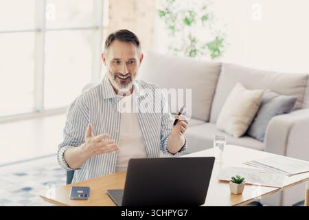 Homme d'affaires mature s'engageant dans une conférence en ligne de la maison avec un ordinateur portable, discutant des questions professionnelles en toute confiance Banque D'Images
