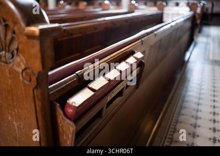Petits livres bibliques dans une étagère au dos de bancs en bois vides à l'intérieur de l'église en Europe. Gros plan, photo grand angle, personne Banque D'Images