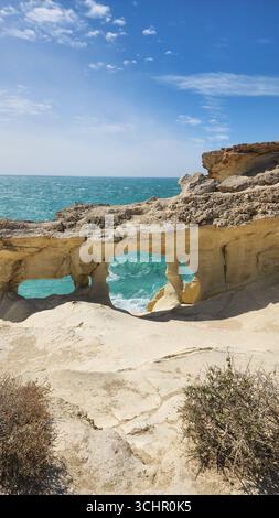 Une vue côtière à couper le souffle encadrée par une arche rocheuse, avec la mer qui s'écrase en dessous et un ciel lumineux en arrière-plan. Banque D'Images