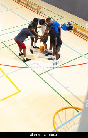 Divers coéquipiers masculins se blottissant au basket-ball sur un terrain de sport en bois franc avec bancs, sac de sport Banque D'Images