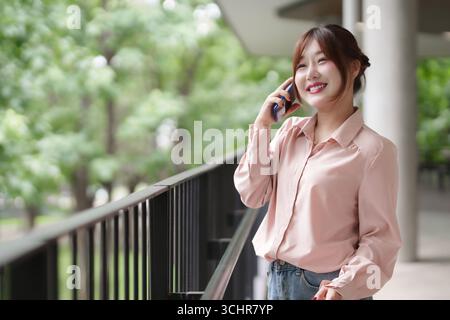 La femme adulte asiatique mène un appel d'affaires en dehors de la gestion joyeuse du style de vie de travail à distance. La technologie de communication moderne la relie dans un environnement naturel Banque D'Images