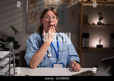 Infirmière fatiguée et stressée travaillant pendant des heures à l'expertise médicale dans le bureau de l'hôpital, dactylographiant le rapport du patient sur ordinateur. Assistant examinant Medi Banque D'Images