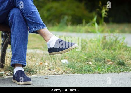 Se reposer pendant la promenade dans une ville : homme en denim et chaussures confortables assis sur le banc du parc. Concept de mode de vie sain, voyage de week-end, détox numérique Banque D'Images