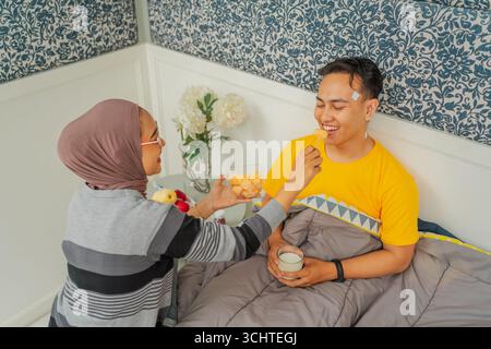 Moment tendre Un couple aimant profite du petit déjeuner au lit, créant des souvenirs spéciaux Banque D'Images