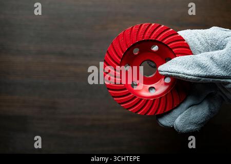 Main d'ouvrier dans des gants de construction tenant le nouveau disque diamant rouge pour meuler le béton, gros plan, espace de copie Banque D'Images