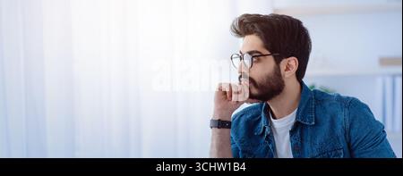 Réfléchi freelance arabe notant des idées à bloc-notes, prenant des notes, assis sur le lieu de travail avec un ordinateur portable, espace de copie Banque D'Images