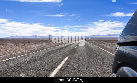 Avant de la plus grande voiture tout en conduisant sur la route pavée droite traversant le paysage désertique à Atacama, région Tarapacá au Chili. Voyager, Road trip. Banque D'Images