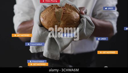 Baker portant une chemise blanche tenant du pain enveloppé de serviette dans le studio, avec des icônes flottantes de médias sociaux Banque D'Images