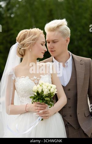 Couple partageant un moment romantique dans la tenue de mariage au milieu de la toile de fond verte Banque D'Images