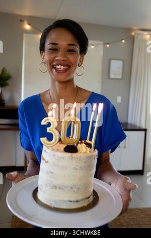 Célébrant 30e anniversaire, femme tenant un gâteau avec des bougies allumées, à la maison Banque D'Images