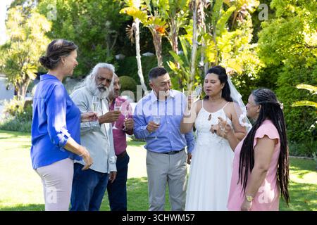 Célébrant dans le jardin, diverses personnes âgées avec champagne s'engageant dans une conversation de mariage animée Banque D'Images
