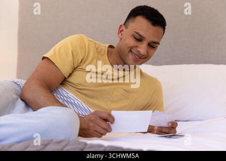 Homme souriant se relaxant sur le lit, regardant des photos, se sentant nostalgique, à la maison Banque D'Images
