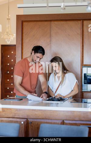 Couple examinant des documents ensemble dans une cuisine moderne, souriant et collaborant Banque D'Images