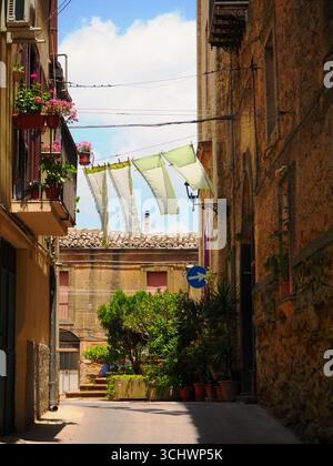 Rue étroite à Enna avec buanderie suspendue, murs en pierre, pots de fleurs et charme méditerranéen dans la ville historique sicilienne, Italie Banque D'Images