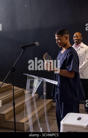 Jeune homme en gommage tenant le prix au podium, souriant avec un collègue à proximité Banque D'Images
