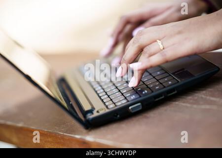 Gros plan de mains tapant activement sur le clavier d'un ordinateur portable dans un espace de travail confortable Banque D'Images