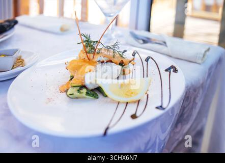 Élégant plat de fruits de mer avec poisson grillé, légumes vibrants et une tranche de citron, magnifiquement disposés sur une assiette blanche, mettant en valeur la créature culinaire Banque D'Images