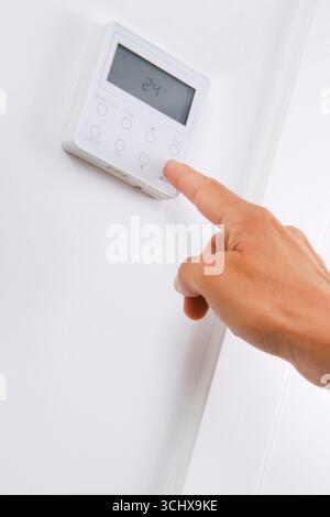 un homme appuie sur le bouton d'un panneau de commande de climatisation réglé à 24 degrés celsius en mode refroidissement, allumant ou éteignant l'unité pour réguler la température Banque D'Images