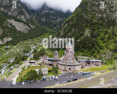 Une grande église en brique rouge se trouve pittoresque dans une vallée montagneuse sous les nuages, vue aérienne, complexe du monastère de Dariali, situé dans la gorge de Dariali Banque D'Images