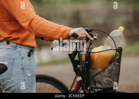 Gros plan d'une personne tenant un guidon de vélo avec un panier rempli de produits d'épicerie Banque D'Images