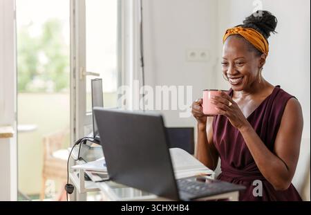Femme heureuse buvant du café et utilisant un ordinateur portable à la maison Banque D'Images