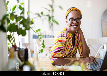 Femme souriante utilisant un ordinateur portable tout en étant assis au bureau dans le bureau Banque D'Images