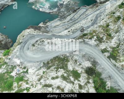Vue aérienne de la carrière de calcaire avec camion lourd se déplaçant le long de la route sinueuse pendant les opérations minières, mettant en évidence l'approvisionnement en matières premières, industriel Banque D'Images
