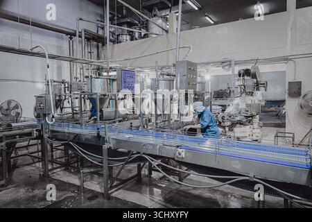 Usine silencieuse, peu de travailleurs de l'usine nettoyant la chaîne de production transportent la bande se préparent à fermer l'usine alimentaire la nuit Banque D'Images