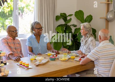 Amis seniors appréciant la conversation et les collations autour de la table à manger à la maison Banque D'Images
