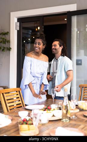 Jeune couple multiracial profitant sur le patio brunch, souriant et bavardant à la table en bois Banque D'Images