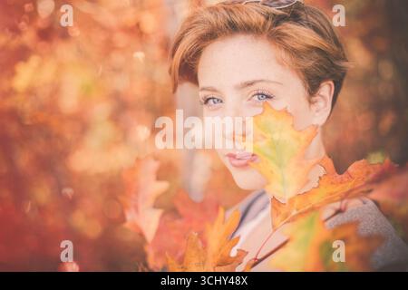 femme souriante aux cheveux rouges avec des feuilles d'automne, portrait Banque D'Images