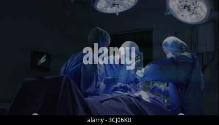 Équipe chirurgicale de travail en bleus bleus et masques effectuant la chirurgie en salle d'opération, avec moniteurs Banque D'Images