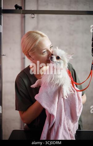 Jeune femme caucasienne adulte séchant un petit chien après le bain au salon de toilettage Banque D'Images