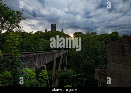 Les anciennes tours et pinacles s'élèvent au-dessus d'une canopée d'arbres au coucher du soleil avec une passerelle traversant la rivière Wear, Durham, Angleterre. Banque D'Images