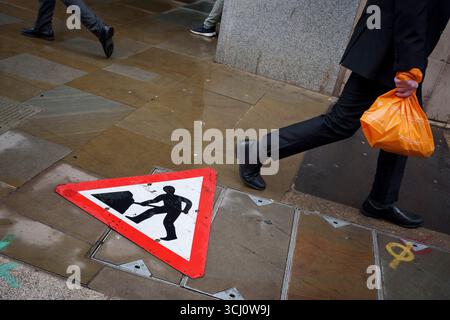 Les employés de la ville passent devant une pancarte de préposé aux travaux routiers qui se trouve à plat sur un trottoir dans la City de Londres, le quartier financier de la capitale, le 4 septembre 2025, à Londres, en Angleterre. Banque D'Images