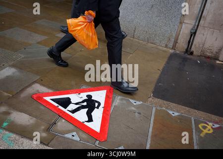 Les employés de la ville passent devant une pancarte de préposé aux travaux routiers qui se trouve à plat sur un trottoir dans la City de Londres, le quartier financier de la capitale, le 4 septembre 2025, à Londres, en Angleterre. Banque D'Images