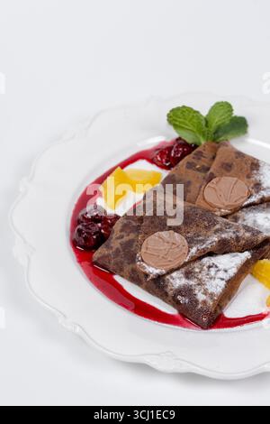 Gros plan détaillé de crêpes au chocolat avec cerises, tranches d'orange, feuilles de menthe et sucre en poudre. Idéal pour la publicité de desserts et la photographie alimentaire Banque D'Images