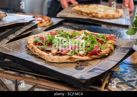 Pizza maison avec prosciutto croustillant et roquette fraîche, magnifiquement présentés sur des planches de bois rustiques, créant une atmosphère chaleureuse et accueillante Banque D'Images