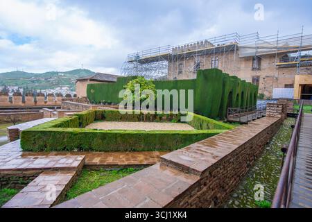 Une vue sur les vastes jardins et les éléments architecturaux de l'historique palais de l'Alhambra à Grenade, en Espagne, par une journée couverte avec des chemins de pierre mouillés Banque D'Images