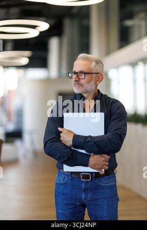 Homme d'affaires professionnel d'âge moyen portant costume tenant l'ordinateur dans le bureau Banque D'Images