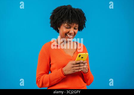 Femme joyeuse s'engageant joyeusement avec son smartphone, absorbée par du contenu divertissant sur son appareil mobile, incarnant la joie du numérique Banque D'Images