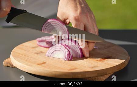 le chef coupe l'oignon rouge frais sur une planche à découper pour préparer un repas sain. cuisine extérieure, gros plan sur la nourriture Banque D'Images