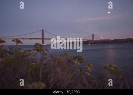 Une vue panoramique époustouflante du fleuve Tage, avec l'emblématique pont rouge 25 de Abril et le lointain monument Cristo Rei. La photographie capture Banque D'Images