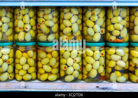 Bocaux d'olives vertes marinées sur l'affichage. Bocaux en verre remplis d'olives vertes conservées dans la saumure, soigneusement empilés avec des couvercles verts, créant un coloré Banque D'Images