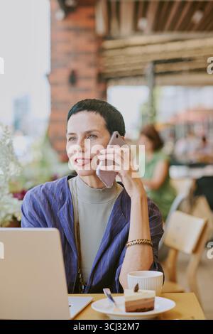 Femme d'âge moyen parlant sur smartphone tout en travaillant au Café Banque D'Images