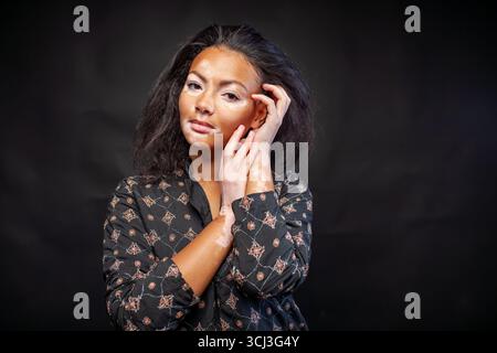 Femme en kurta traditionnel debout sur fond noir. Jeune dame avec des troubles cutanés de vitiligo regardant la caméra dans le studio Banque D'Images