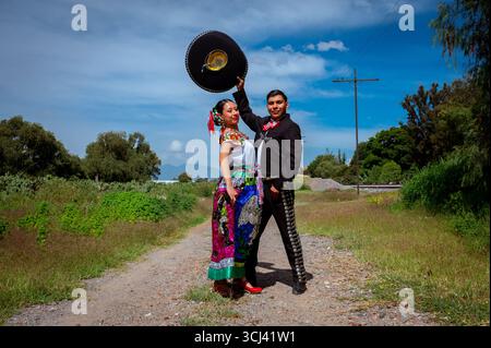 Couple mexicain posant à l'extérieur en costumes folkloriques, avec l'homme portant un costume charro et sombrero et la femme dans une robe brodée colorée Banque D'Images